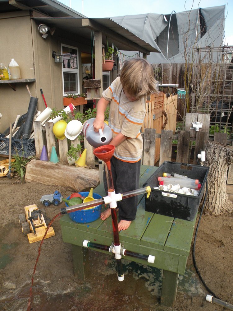 Child experimenting with water flow using pipes and funnels during a hands-on STEM activity at an outdoor school.