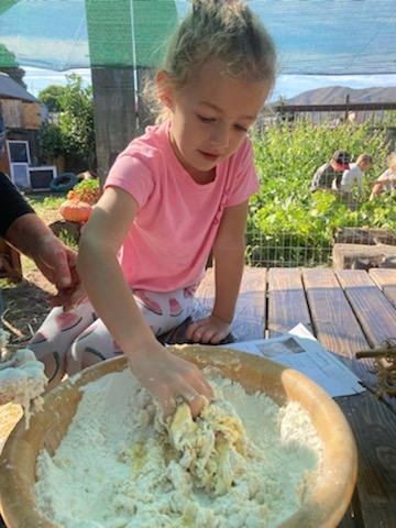 Child learning hands-on skills by kneading bread dough at a nature-based outdoor school.